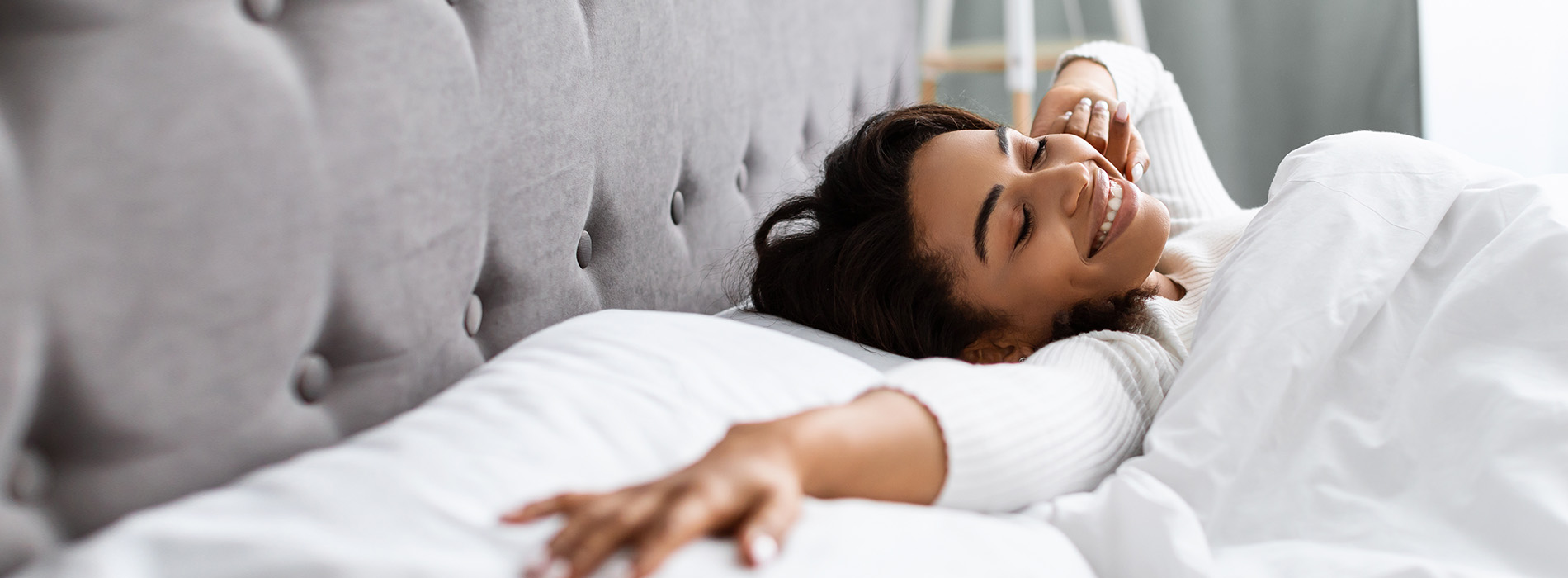 A woman is lying down on a bed, smiling and looking upwards.