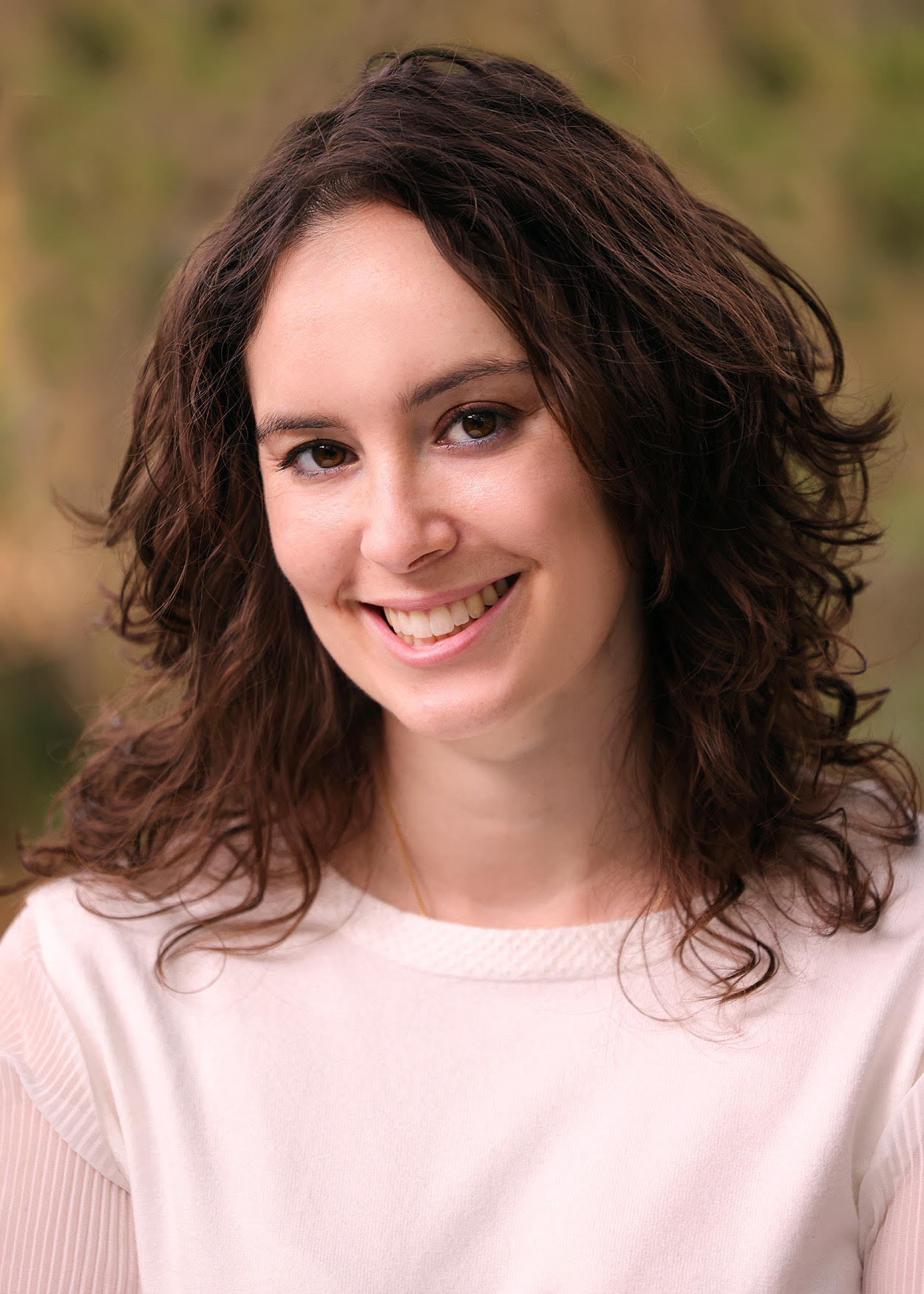 The image is a portrait of a woman with short brown hair, wearing a white top and smiling at the camera.