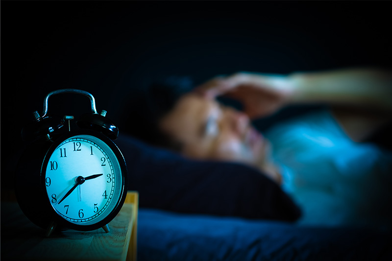 An alarm clock with a glowing face, set against a dark background, signifies the passing of time in a bedroom setting.