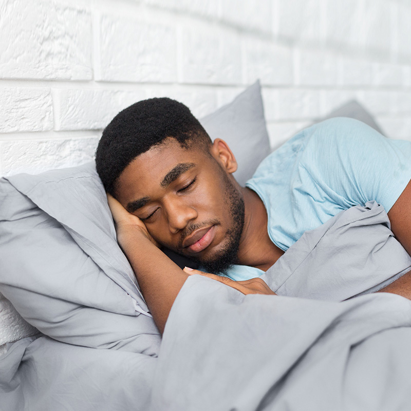 A man is lying in bed, his eyes are closed and he appears to be asleep.