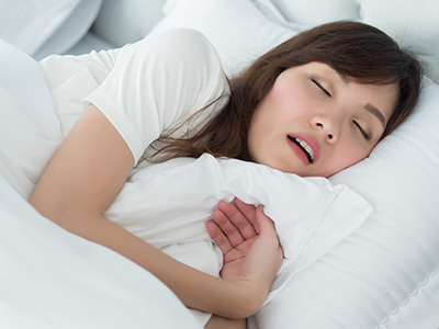 A young woman with her eyes closed, lying in bed with a pillow and blanket, appears to be asleep.